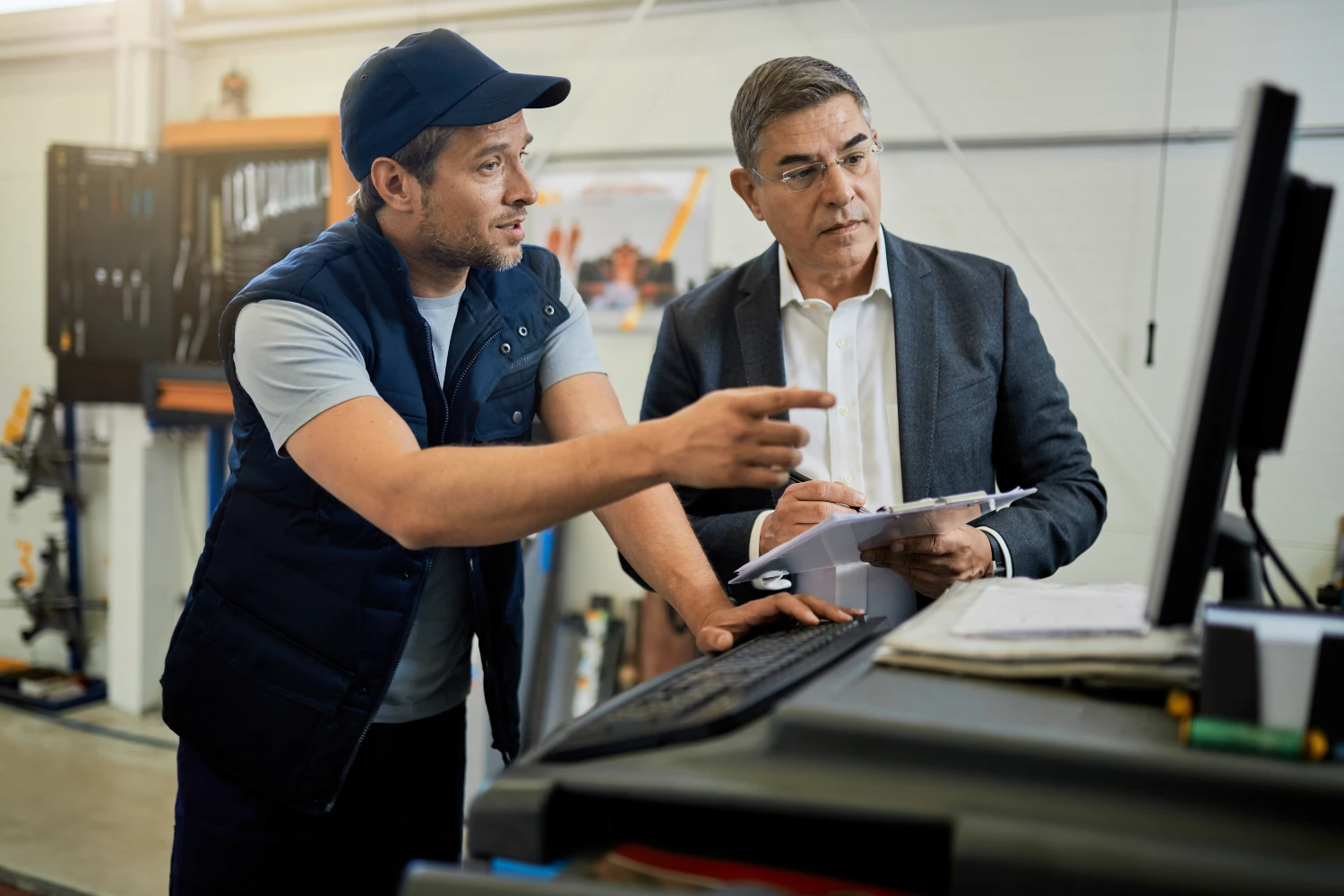 mid-adult-manager-car-mechanic-talking-while-using-computer-auto-repair-shop